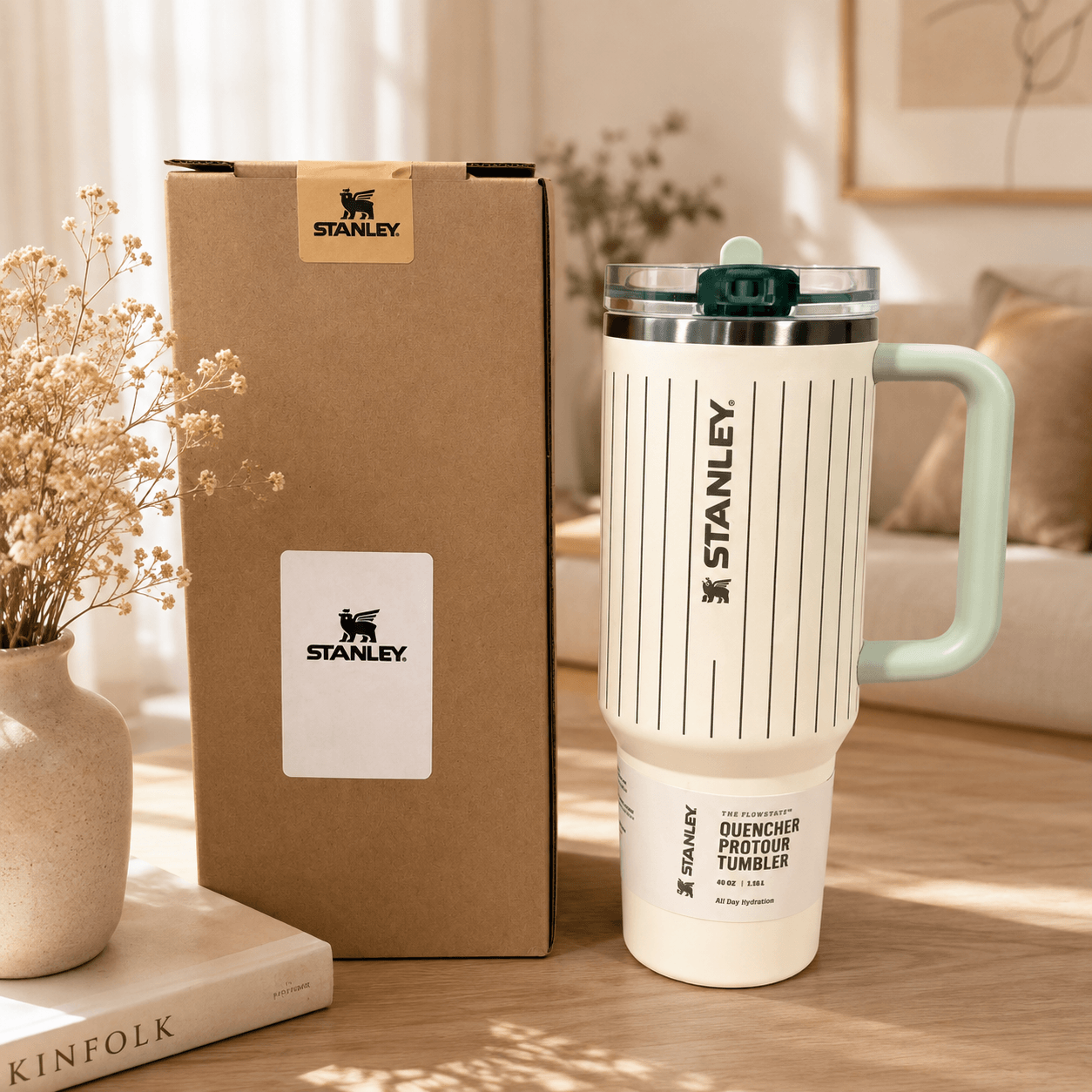 A Stanley duquencher pourtour tumbler in off-white with black vertical stripes and a mint green handle, shown next to its brown cardboard packaging box on a wooden table.