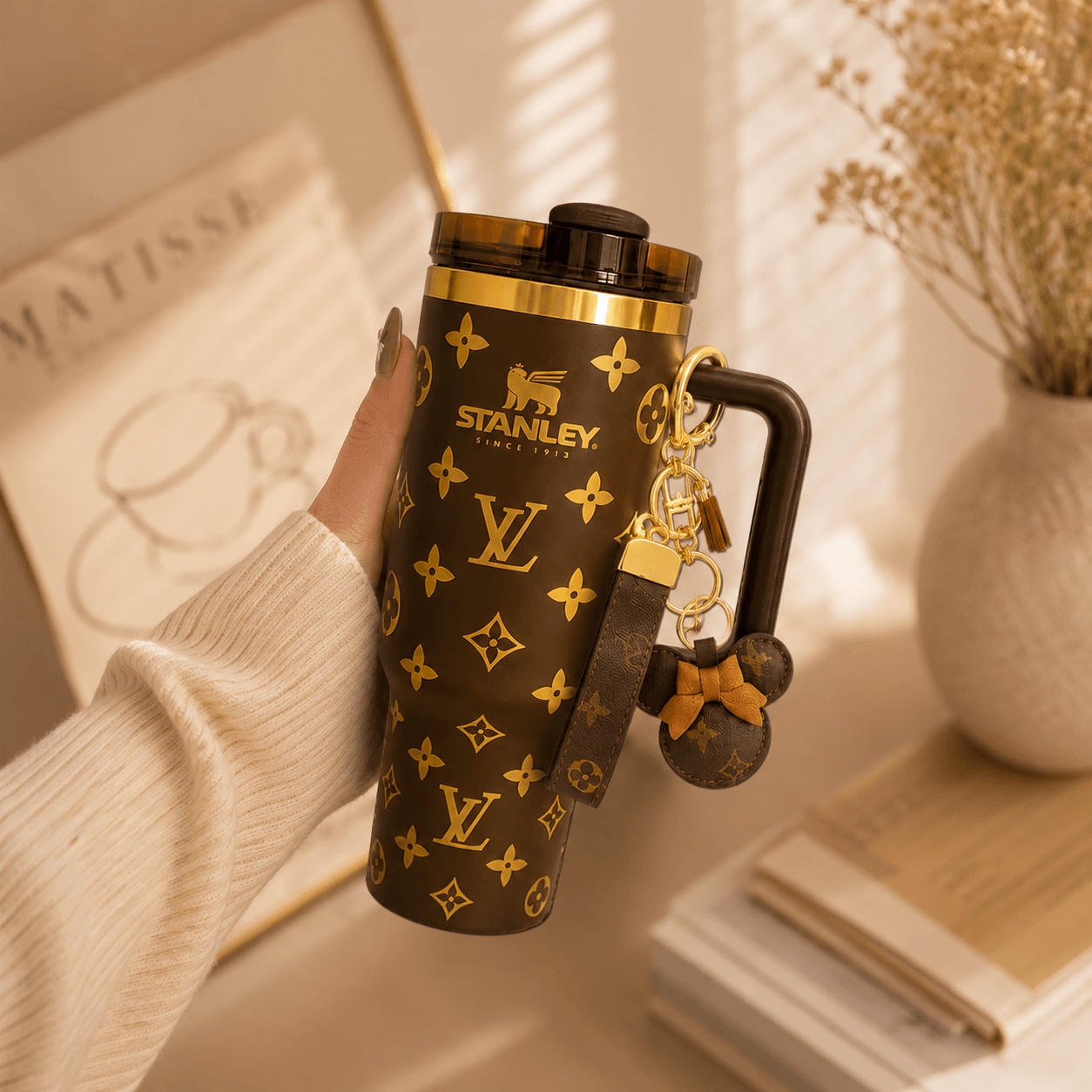 Hand holding a Stanley tumbler with Louis Vuitton monogram design, featuring a keychain.