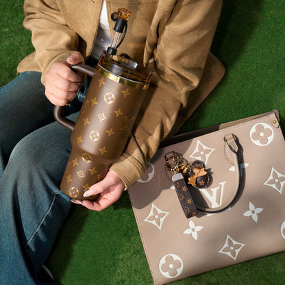 Person holding a brown patterned thermos with a matching handbag on a green surface