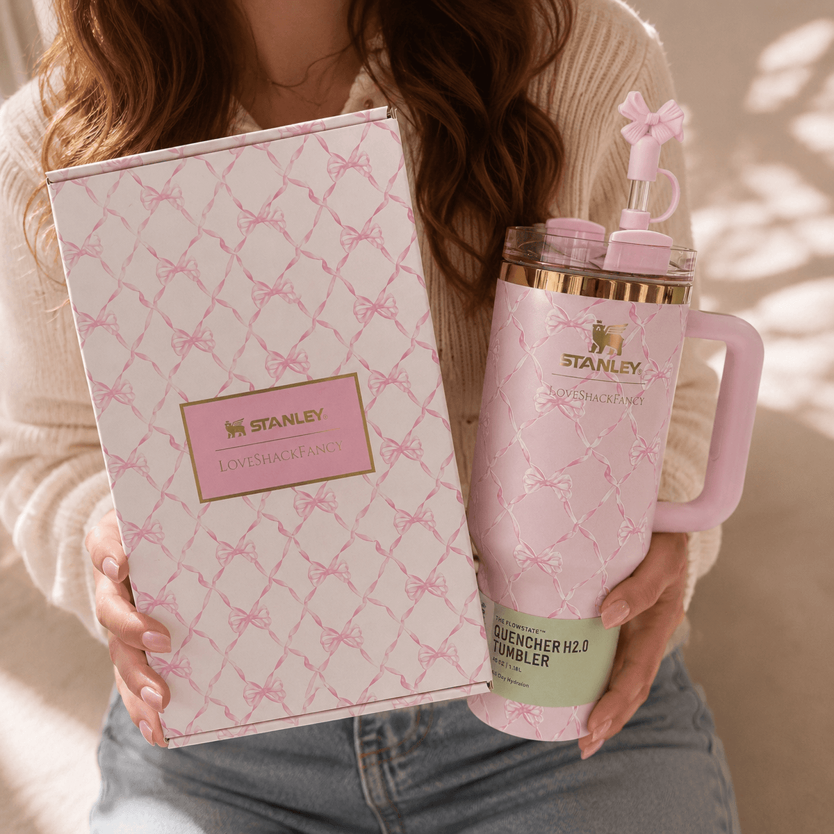 Person holding a pink Stanley tumbler and packaging with a bow design.