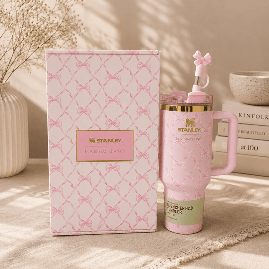 Pink Stanley tumbler with decorative lid next to its packaging on a neutral background