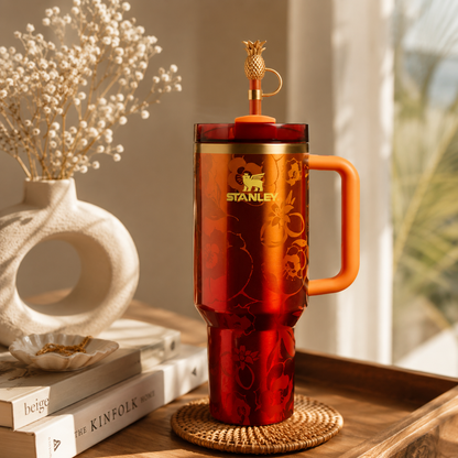 Red Stanley mug with orange handle on a wooden surface with books and decor.