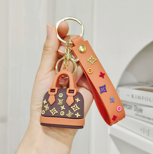 Hand holding a keychain with a small handbag design and colorful accents.