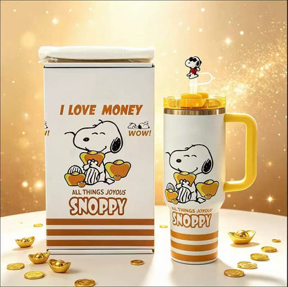 A white Snoopy tumbler with a yellow handle and lid, shown next to its matching white box packaging. The packaging and tumbler feature a cartoon print of Snoopy holding gold ingots with the text 'I LOVE MONEY', 'ALL THINGS JOYOUS', and 'SNOPPY'.